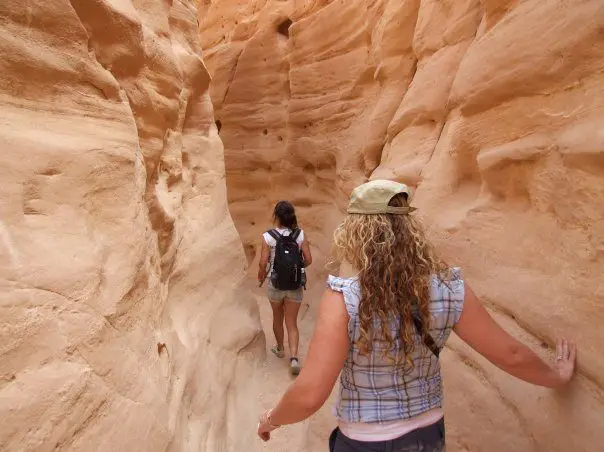 Two girls hiking through a narrow red rock canyon. 