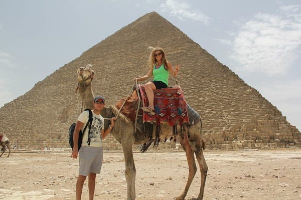 Egypt travel tips. Sitting on a camel in front of the Giza pyramids with a man holding the camels rope. 